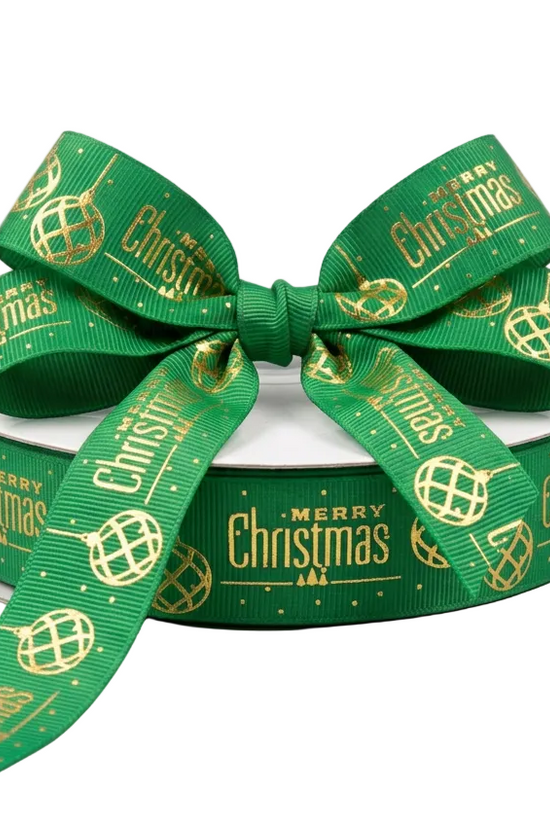 A spool of green Christmas ribbon with a large bow, featuring gold foil text and globe patterns that read 'Merry Christmas'.