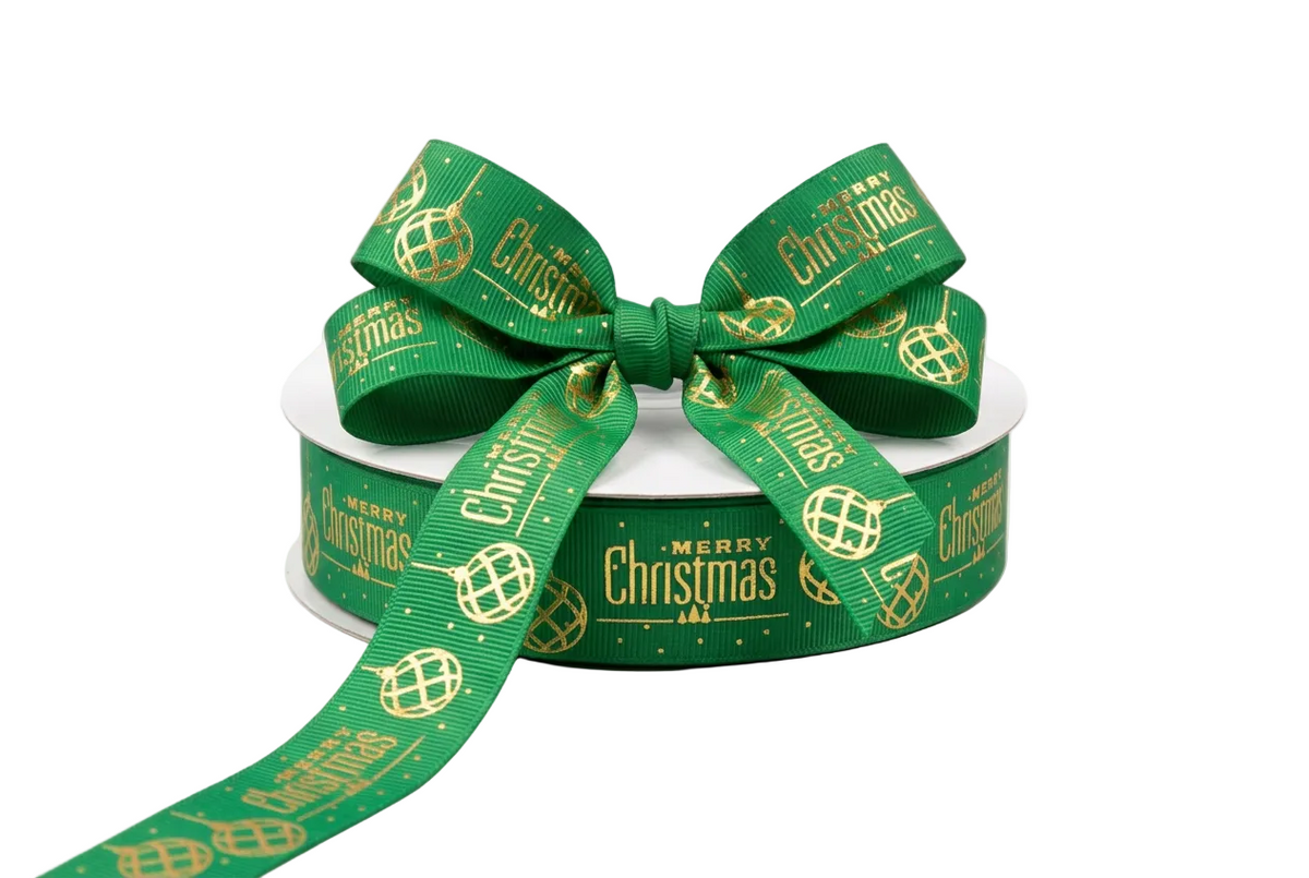 A spool of green Christmas ribbon with a large bow, featuring gold foil text and globe patterns that read 'Merry Christmas'.