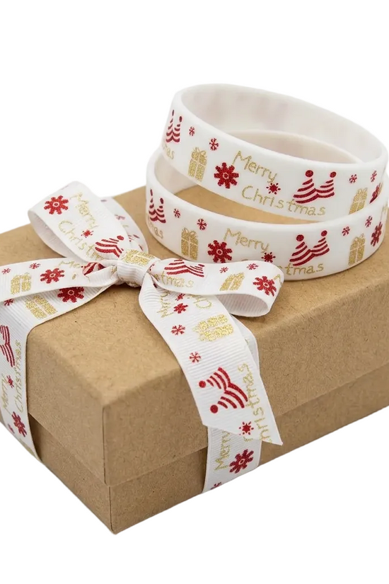 A brown kraft gift box tied with a white Christmas-themed ribbon printed with red snowflakes, gold gift boxes, and 'Merry Christmas' text, with a matching rolled-up ribbon coil placed on top.