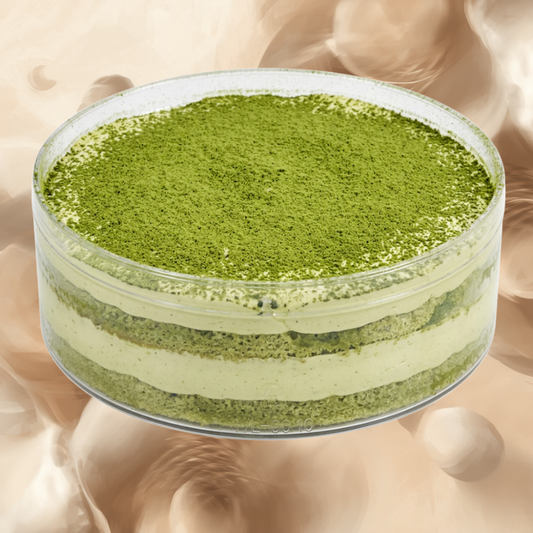 A clear round container holding a layered green dessert, topped with a fine layer of green powder, set against a soft beige abstract background.