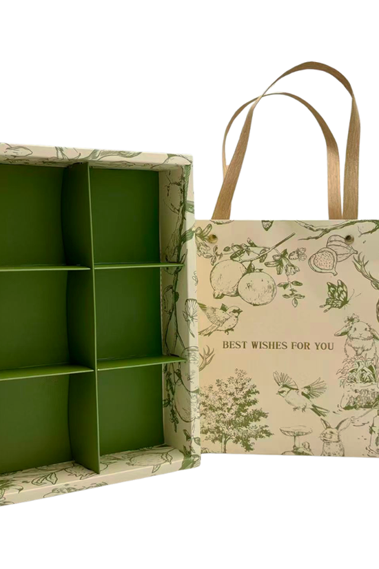 A green and beige illustrated gift box organizer shown open next to its matching paper shopping bag with tan handles. The box has six compartments and a green interior, while the bag features a vintage-style botanical and animal print with the text 'BEST WISHES FOR YOU'.
