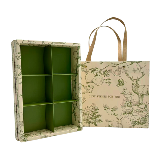 A green and beige illustrated gift box organizer shown open next to its matching paper shopping bag with tan handles. The box has six compartments and a green interior, while the bag features a vintage-style botanical and animal print with the text 'BEST WISHES FOR YOU'.